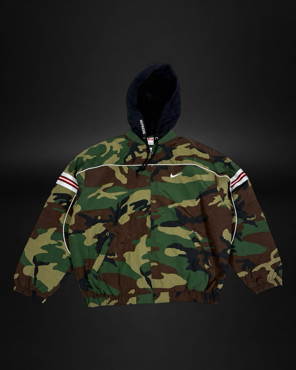 Chaqueta cortavientos Saint Krew con estampado de camuflaje, capucha negra, detalles reflectantes y bandas deportivas.